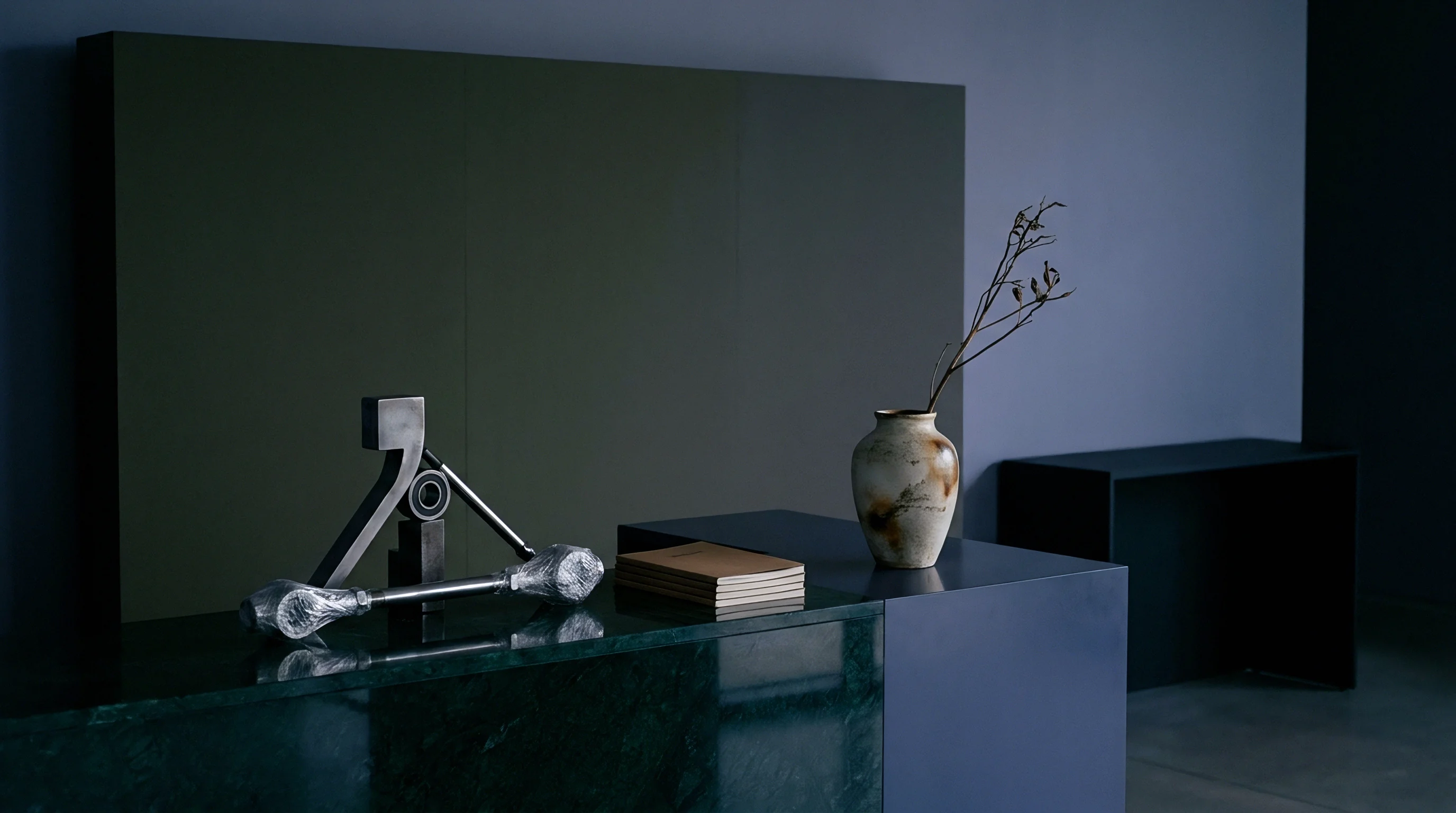 Polished green marble and blue composite surfaces support a metallic geometric sculpture alongside a ceramic vessel and bound documentation.