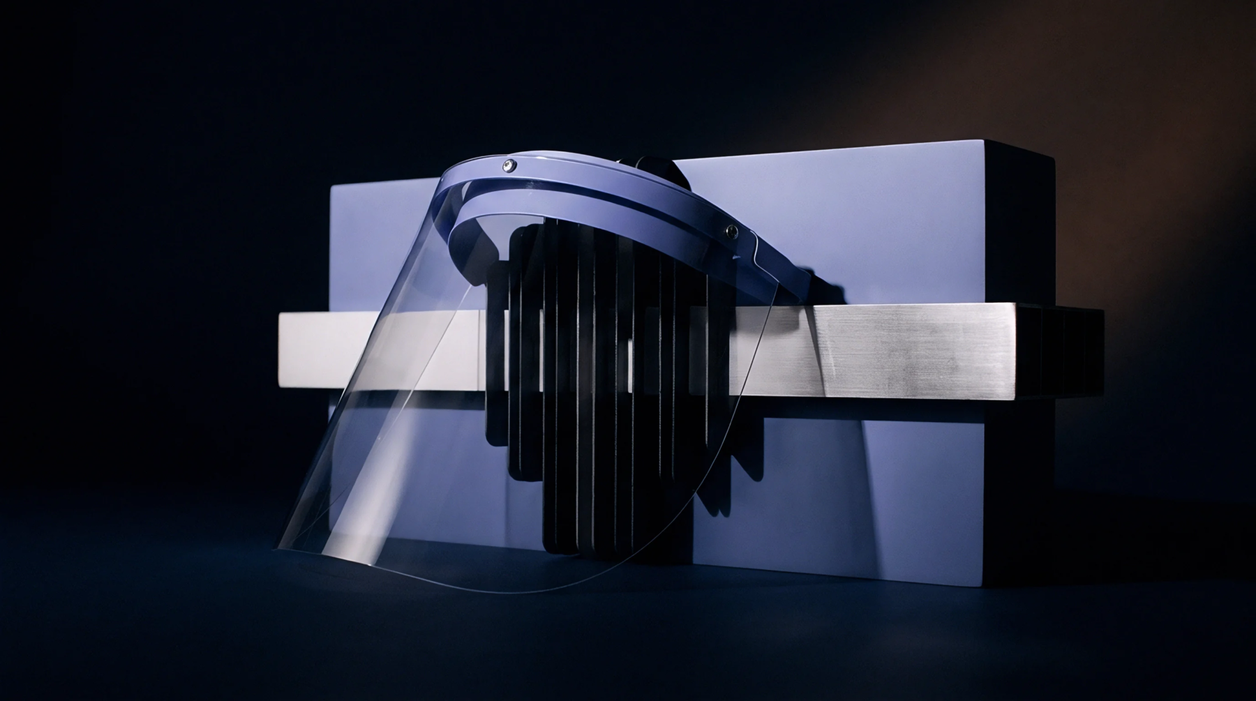 A clear polymer safety visor rests before black vertical cooling fins mounted on blue and silver structural blocks.